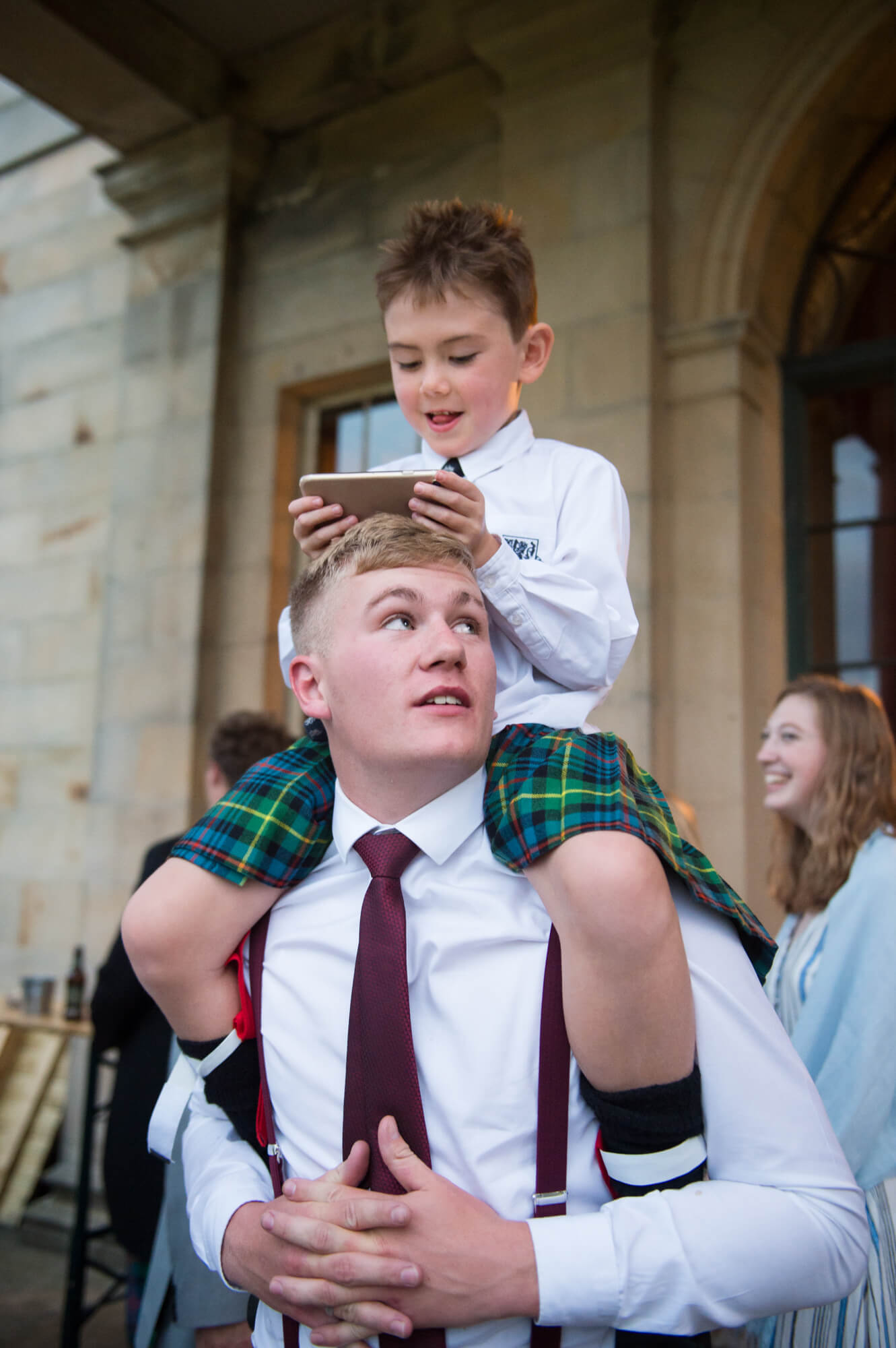 A boy with a kilt sitting on his dads shoulders